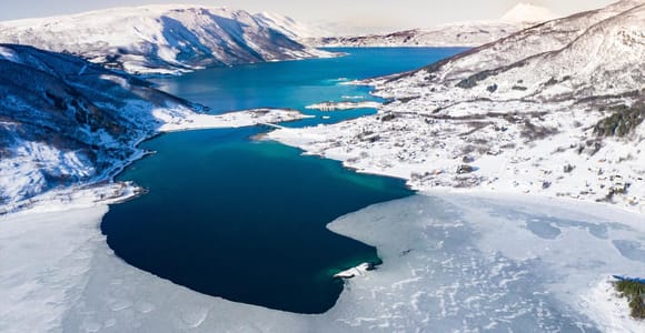 Snow-covered mountains descending towards a dark Norwegian fjord near Narvik