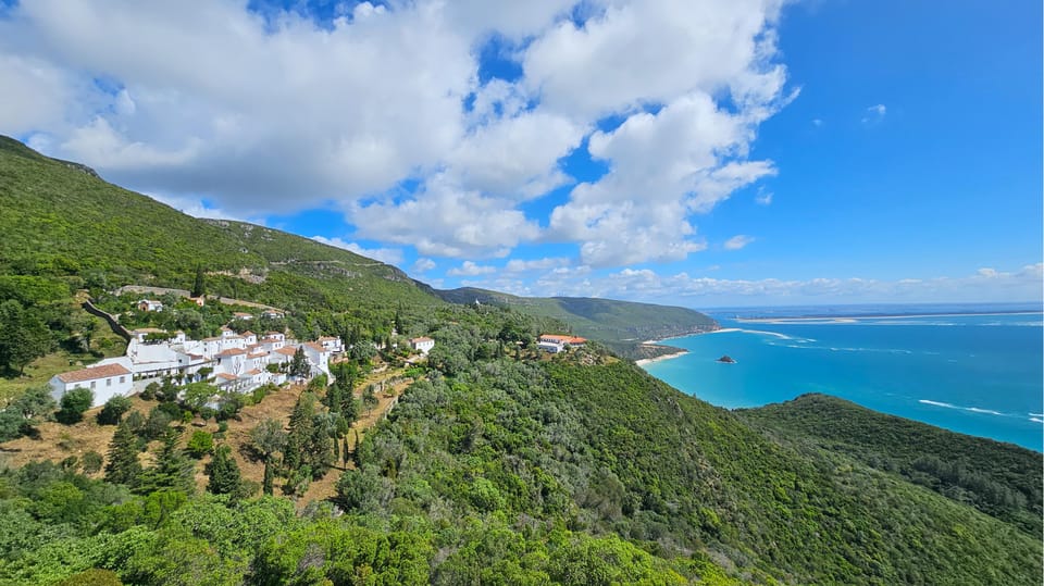 White convent buildings on a green hillside above a turquoise bay and a long sandy spit