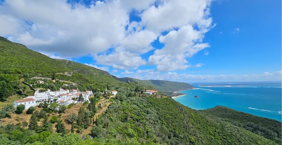 White convent buildings on a green hillside above a turquoise bay and a long sandy spit