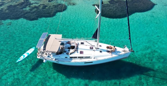 A white sailing yacht at anchor off a rocky, scrubby island in deep blue water under a clear sky