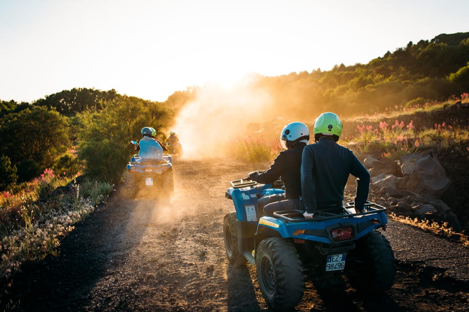 Two riders in helmets on a blue quad bike on a dusty track in low golden light, a second quad behind