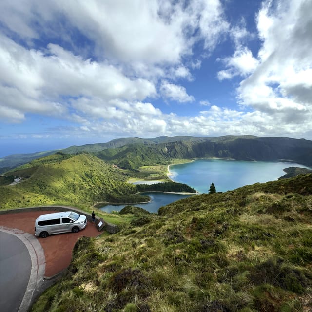 A van parked at a viewpoint above a blue crater lake ringed by green hills