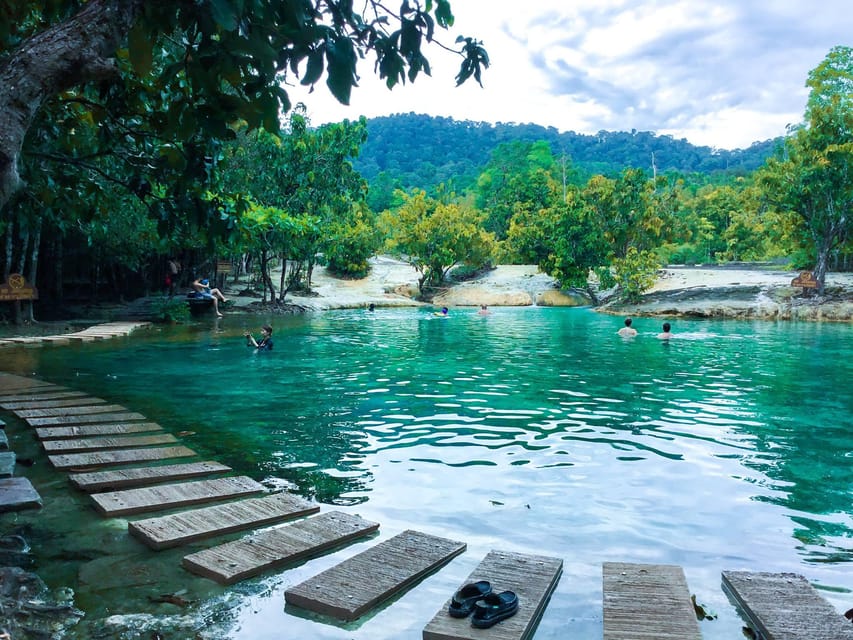 Wooden plank walkway leading into the shallow green water of the Emerald Pool, surrounded by forest