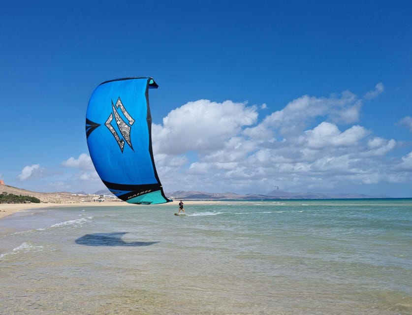 Kitesurfista con una cometa azul sobre aguas costeras poco profundas