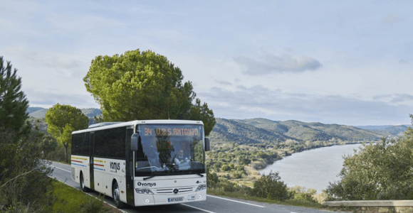 A white Vamus coach on a road above a wooded river valley