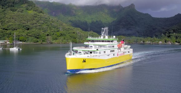 A white passenger ferry with an open upper deck crossing calm water, the green ridgeline of an island low on the horizon behind it