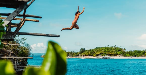 Traveller jumping from a dark limestone ledge into blue tropical water