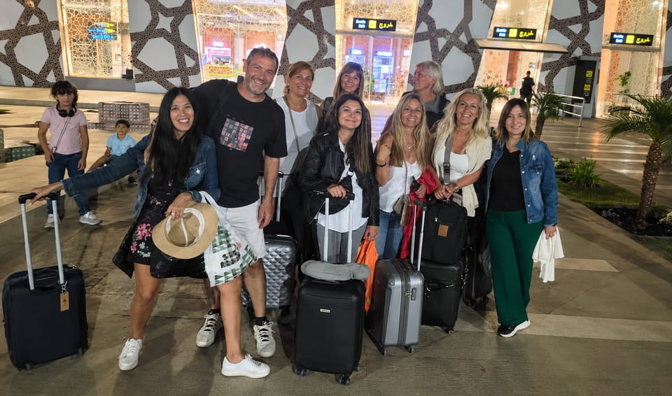 Group of travellers with wheeled suitcases outside an airport terminal in the evening