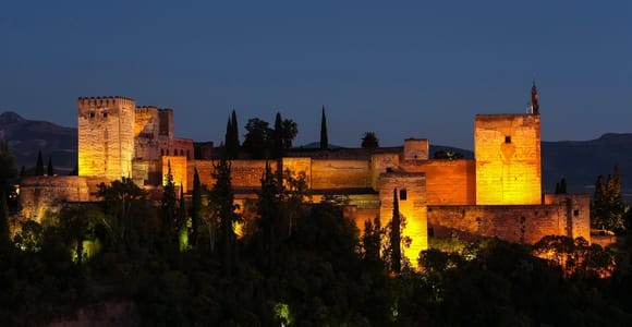 Illuminated colonnades reflected in a dark pool inside the Alhambra at night