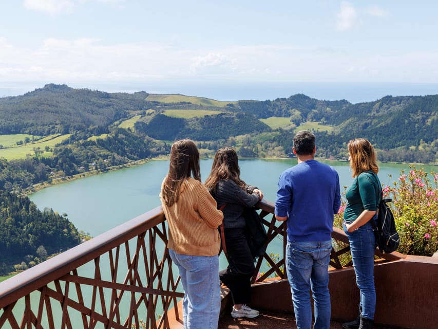 Visitors at a railing looking over a green lake and wooded hills