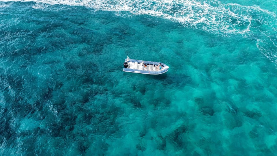 Ein kleines Boot fährt über die kristallklaren Gewässer vor Fuerteventura, umgeben von türkisblauem Wasser und schäumenden Wellen.