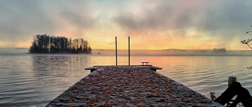 Eine Holzsauna mit aufsteigendem Dampf an einem verschneiten Flussufer in der Abenddämmerung