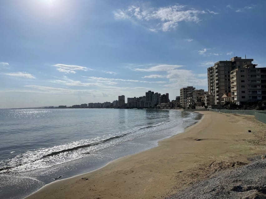 A sandy beach curving along a calm sea, with rows of empty high-rise hotel blocks in the distance under a blue sky