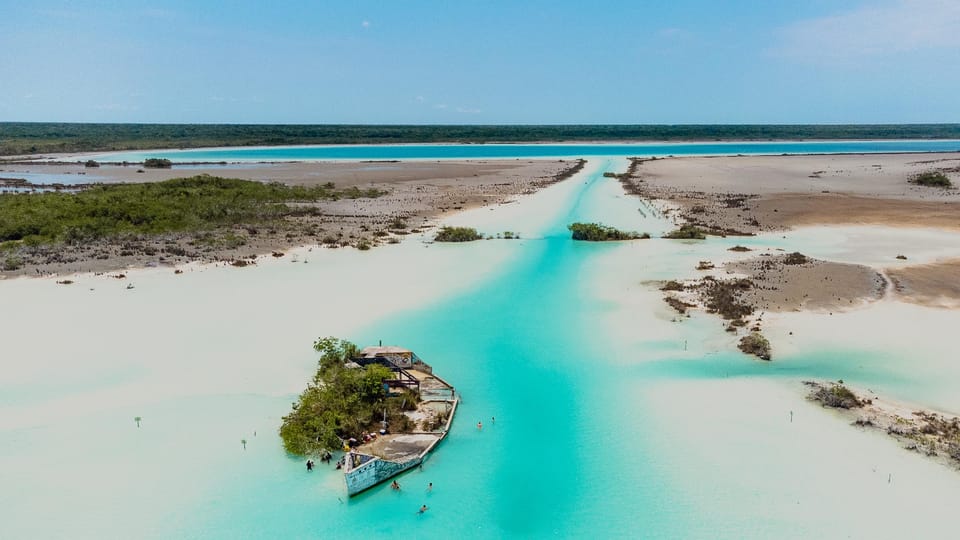 A small boat crossing bands of pale turquoise and deep blue water on Bacalar Lagoon