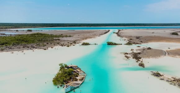 A small boat crossing bands of pale turquoise and deep blue water on Bacalar Lagoon