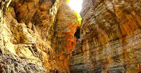 A narrow gorge of layered orange and yellow limestone closing overhead, with a stony path winding through the bottom