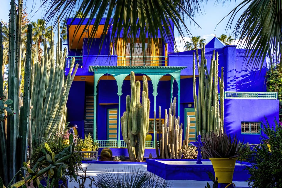 Bâtiment d’un bleu cobalt intense avec un auvent à arcades turquoise, encadré de hauts cactus colonnaires et de palmes