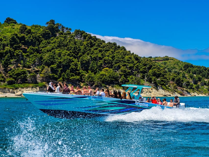 Speedboat full of passengers crossing deep blue water in front of a wooded coastline