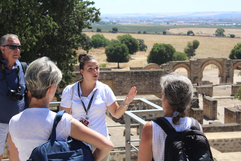 A guide explains the site to a small group above the excavated ruins and horseshoe arches of Medina Azahara