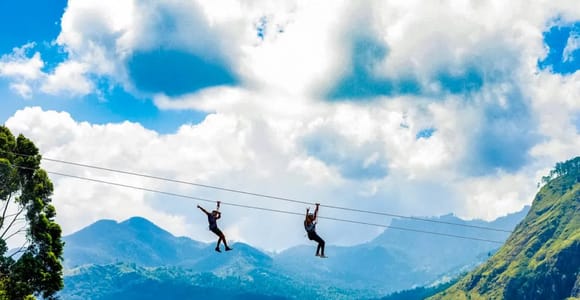A rider suspended over a green tea valley on a twin zipline near Ella