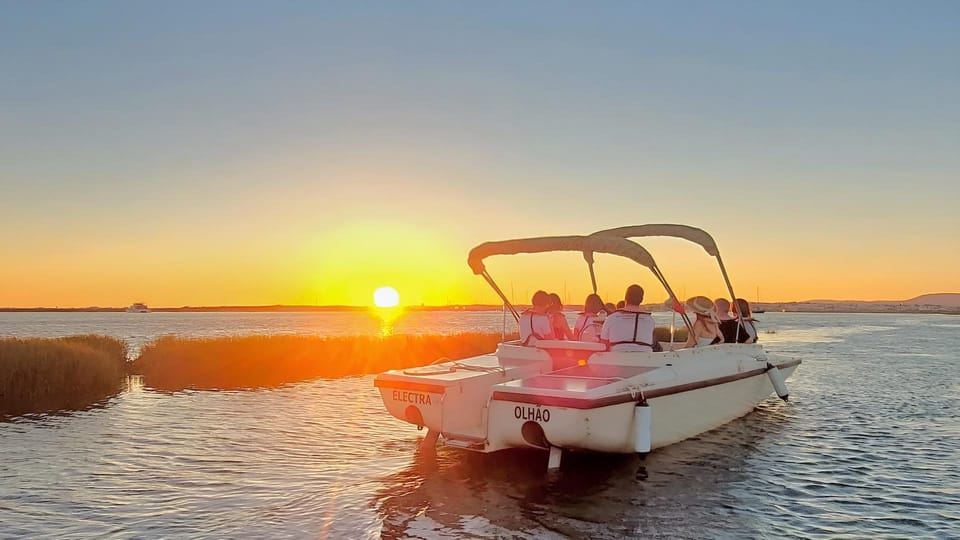 A small boat gliding across the calm Ria Formosa lagoon at sunset