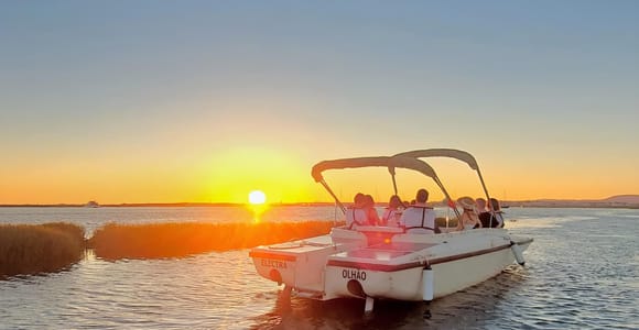 A small boat gliding across the calm Ria Formosa lagoon at sunset