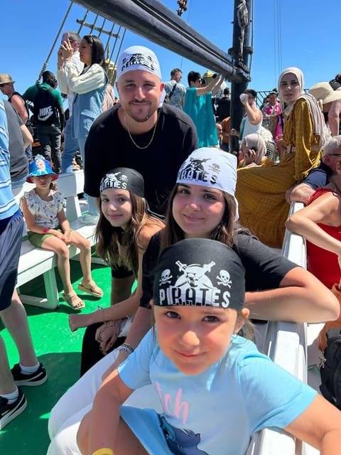 Deux adultes et deux fillettes sur un banc de bateau, tous les quatre coiffés de bandanas de pirate, d’autres passagers derrière eux
