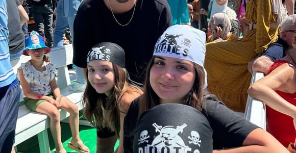 Two adults and two girls on a boat bench, all four wearing pirate bandanas, other passengers behind them