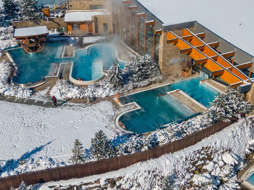 Aerial view of steaming outdoor thermal pools beside snow-covered ground and conifers