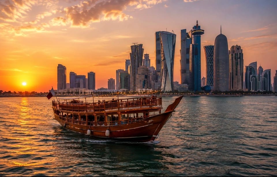 A wooden dhow with warm deck lights sailing past the illuminated Doha skyline