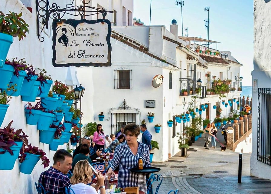 Whitewashed Mijas lane with rows of blue flowerpots on the wall and diners at café tables