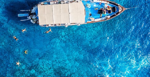 A small excursion boat passing a rocky green cove in the clear water around Ischia
