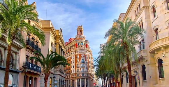 A palm-lined street in Valencia leading to an ornate corner building with a tower
