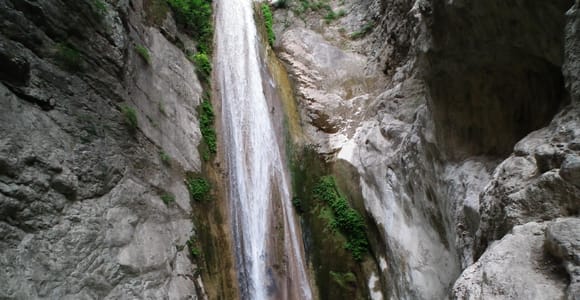 A tall, narrow waterfall dropping into a turquoise rock pool in a grey limestone gorge