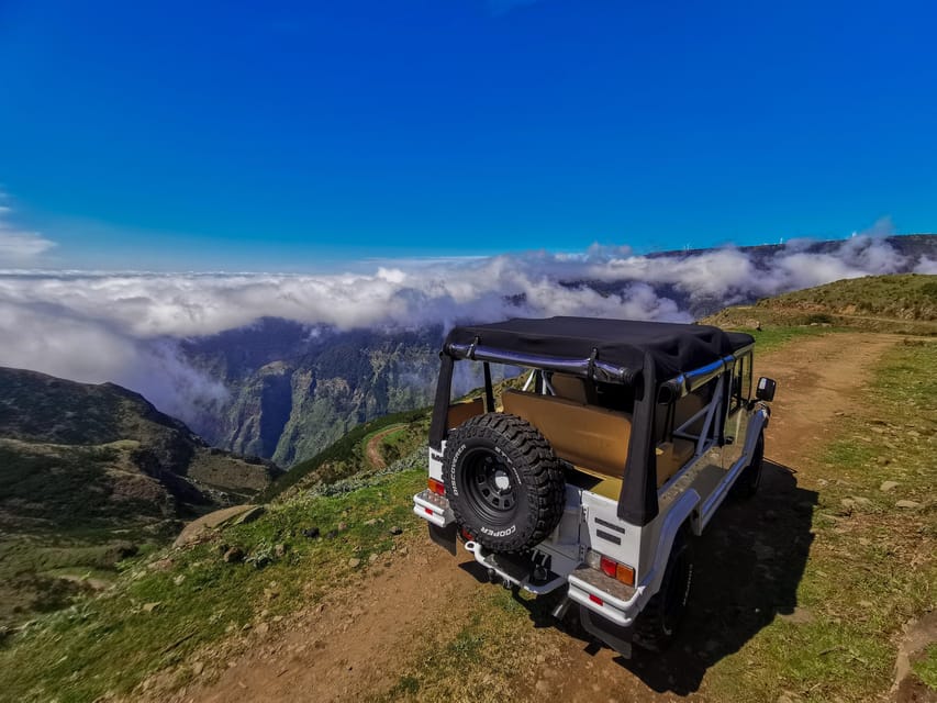 An open-topped off-roader parked on a gravel track high above a valley filled with cloud