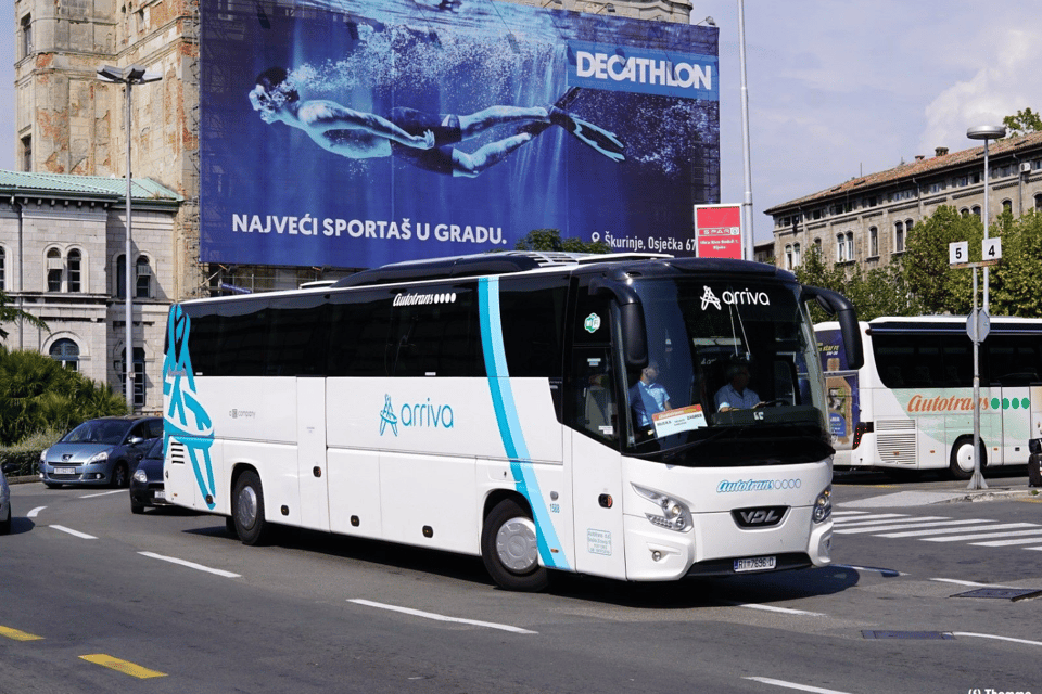 A white coach with blue stripes and the Arriva name driving along a city street past old stone buildings and a large billboard