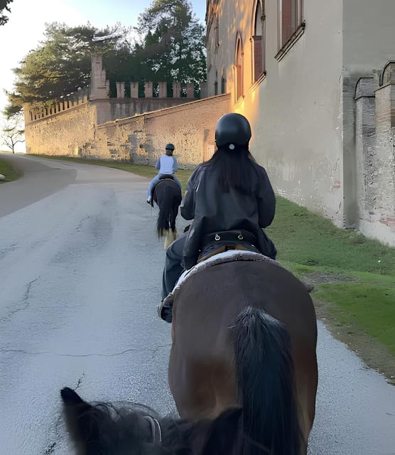 Two helmeted riders on horses on a road beside an old crenellated wall