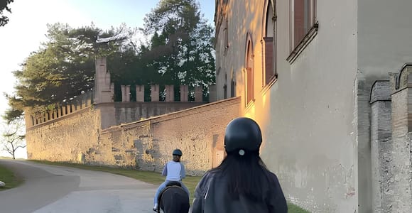 Two helmeted riders on horses on a road beside an old crenellated wall