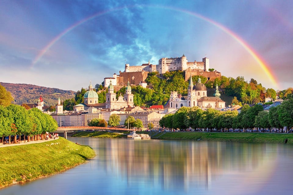 A narrow shopping street in Salzburg's old town lined with tall pastel houses and ornate wrought-iron shop signs
