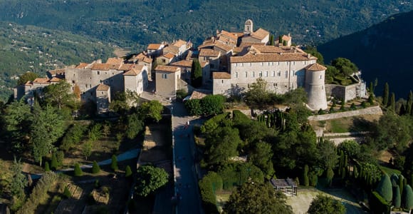 A hill village of stone houses with tiled roofs high above green hills, with the sea beyond