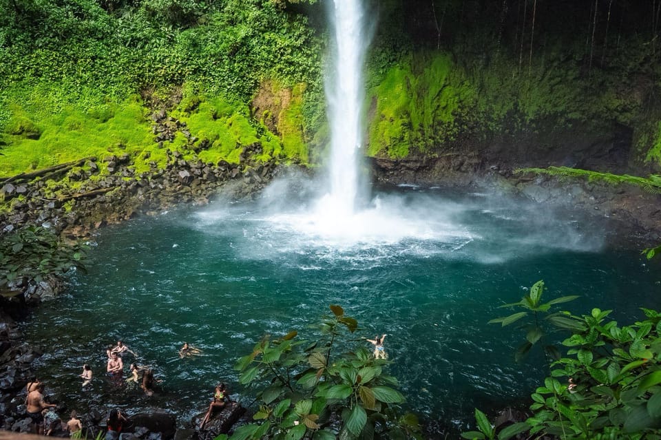 A tall white waterfall dropping into a blue pool surrounded by dense green rainforest