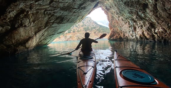 Two sea kayaks crossing clear green water below pale cliffs on southern Naxos