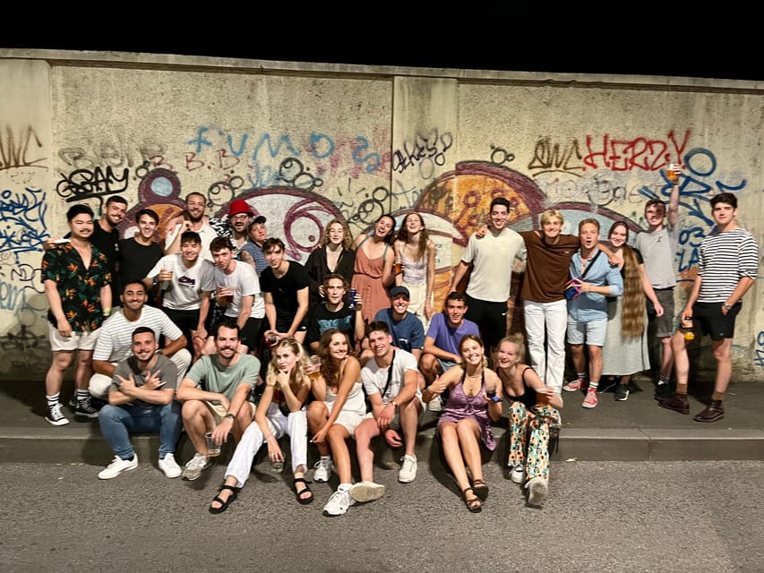 A large group posing at night on a pavement in front of a wall covered in graffiti