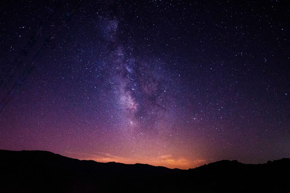 La Vía Láctea sobre una cresta oscura, con la última luz anaranjada del atardecer a lo largo del horizonte